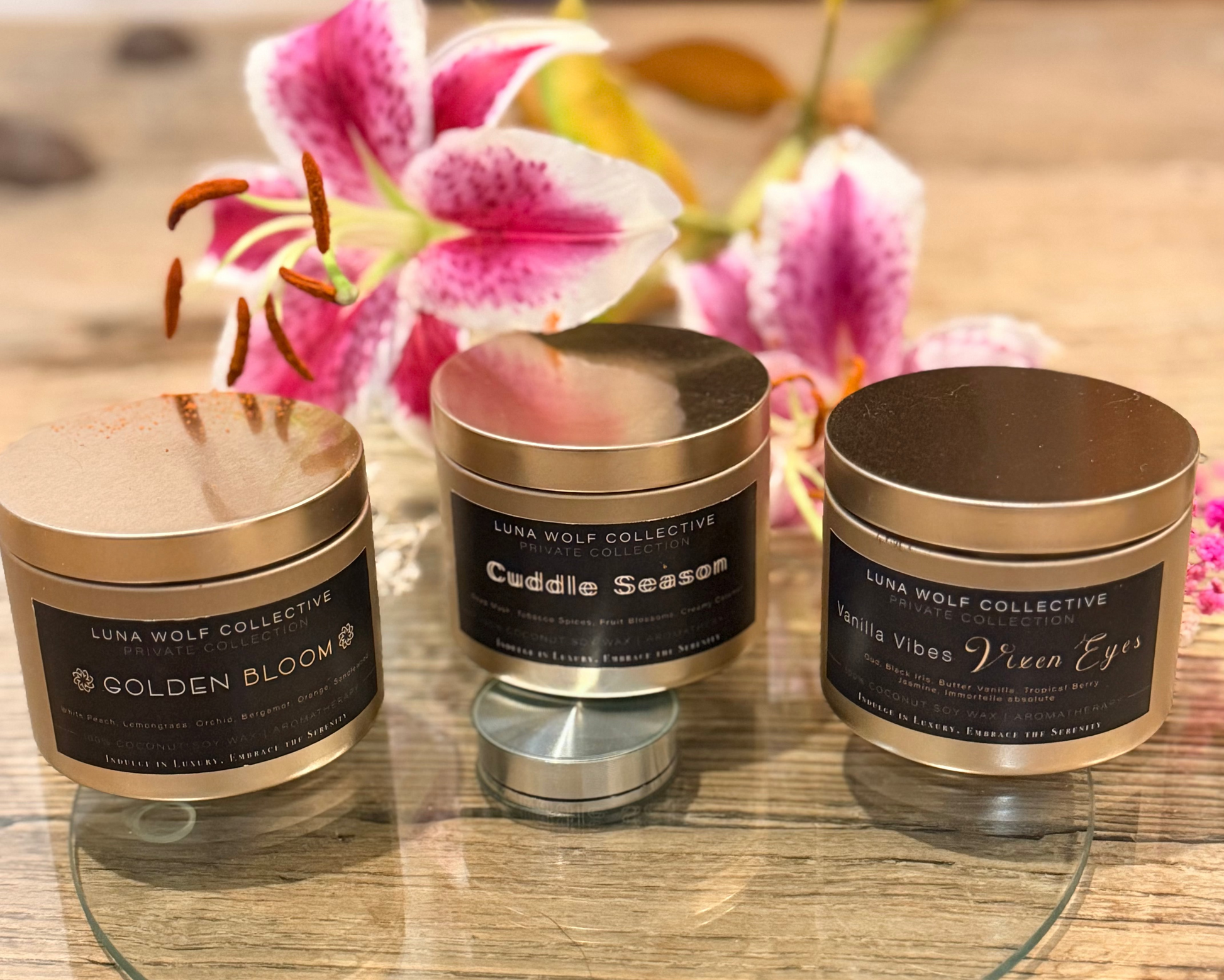 Three small cylindrical containers with labels on a glass surface with flowers in the background