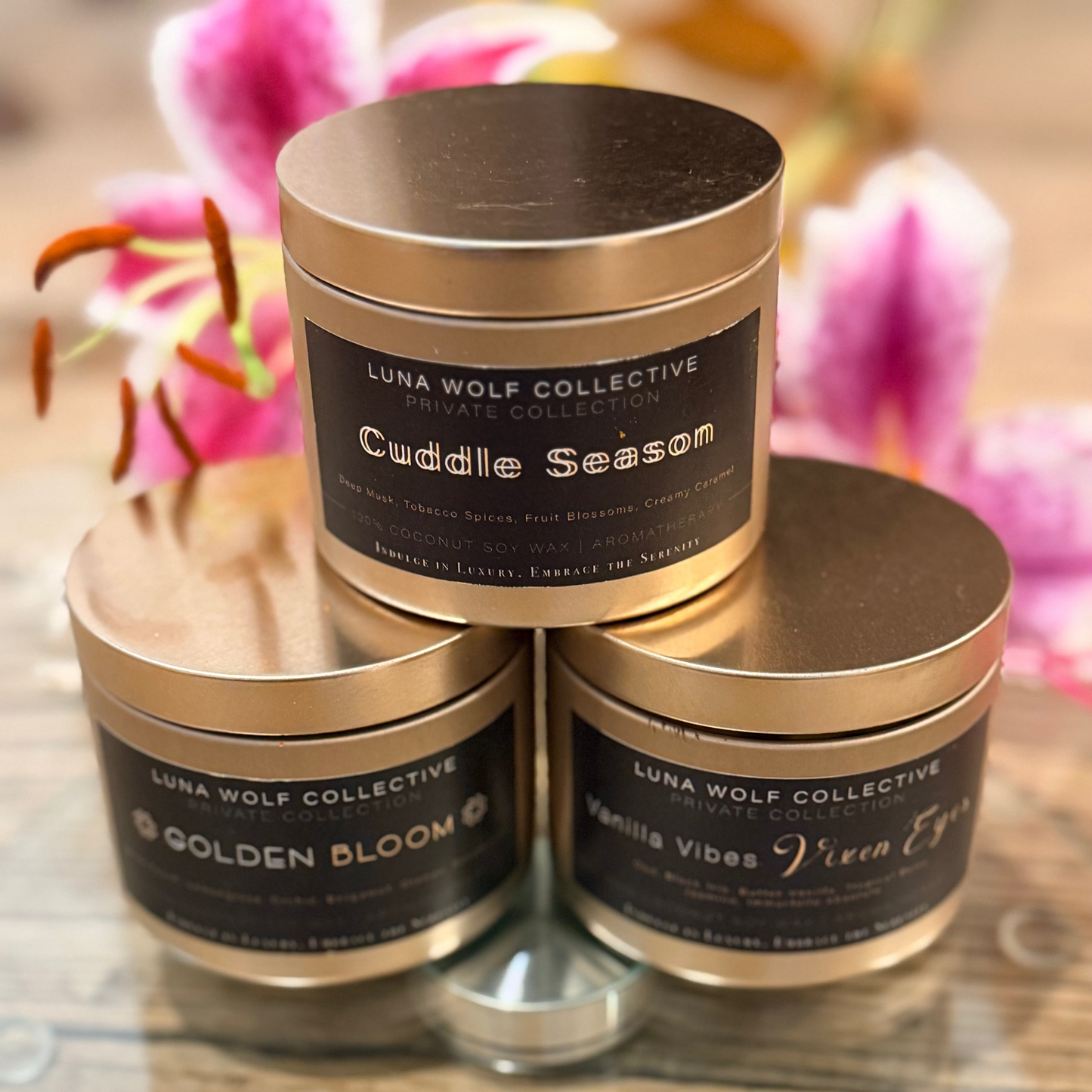 Three cylindrical containers with gold lids and black labels on a wooden surface with blurred flowers in the background.