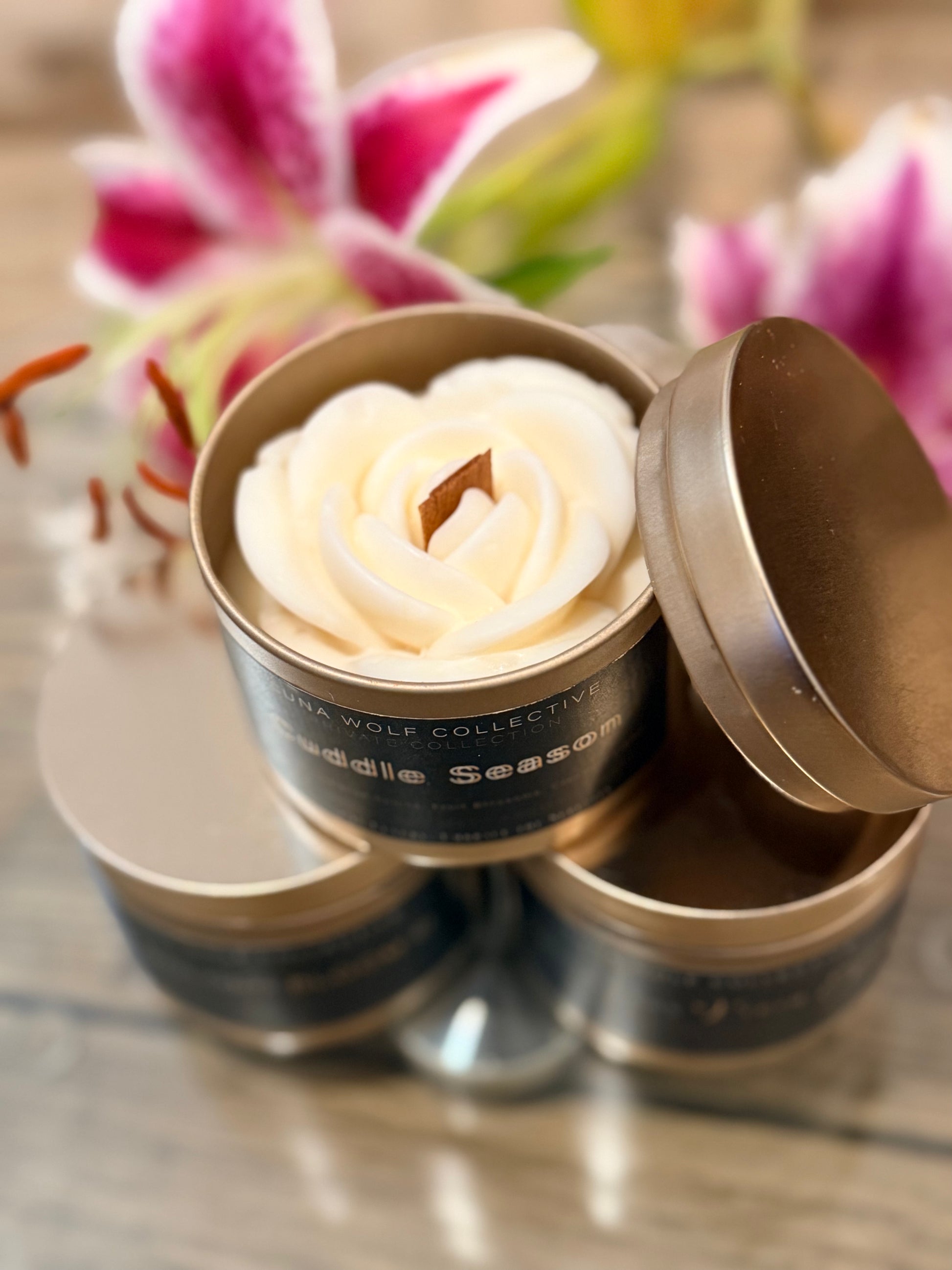 Decorative candle shaped like a rose in a tin container with flowers in the background