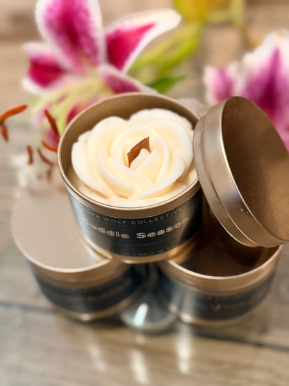 Decorative candle shaped like a rose in a tin container with flowers in the background