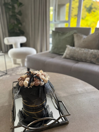 Decorative flower arrangement in a black pot on a mirror tray in a living room.